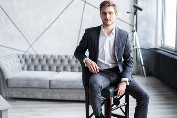 Portrait of confidence. Thoughtful young man in full suit looking away while sitting on the stool.