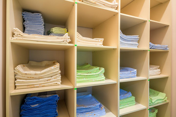 Interior of white plastic cabinet or clothing open wardrobe with stacked piles of clean colorful linen on shelves. Furniture design, hotel, hospital or kindergarten concept.