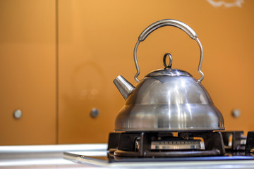 Shiny stainless tea kettle teapot with boiling water on gas stove on kitchen yellow copy space...
