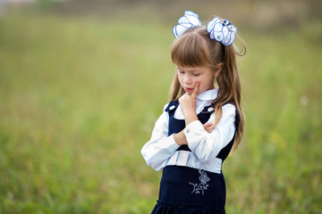 Close-up portrait of cute adorable confident first grader girl in school uniform and white bows in...