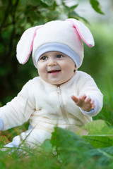 Baby in rabbit costume seating on grass in park and smiling.