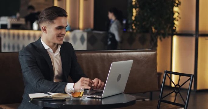 Smiling businessman using laptop computer sitting at the cafe table