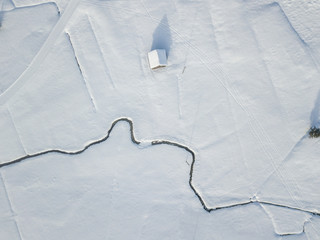 Aerial view of meandering river on snow covered ground. White fields with curved brook flowing...