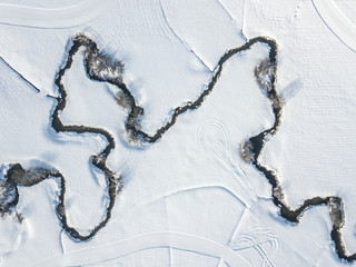 Aerial view of meandering river on snow covered ground. White fields with curved brook flowing...