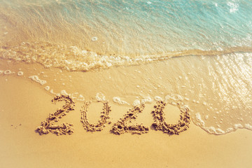 Happy New Year 2020 concept, 2020 number lettering on the sea beach, wave and golden light of sunset.