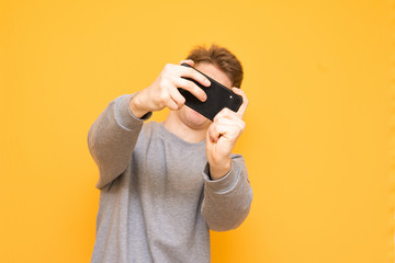 Man plays a game on a smartphone, isolated on a yellow background. Focus on the smartphone. Mobile gaming concept.