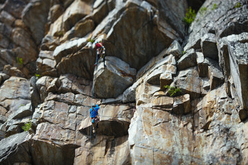 The climber climbs up the rope against the background of a huge rock wall. Two person rope.  Tilt-Shift effect.