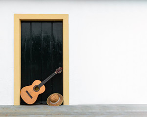 Spanish or classical guitar resting on a door of an andalusian patio, copy space right. Outdoor scene, musical instrument in white wall of rural house. - Powered by Adobe