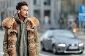 Fashionable man walk outdoors wear  fur jacket with street background - Image