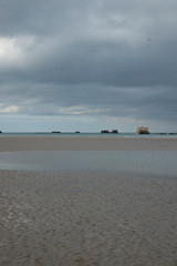 the normandy beaches in france showing ruins and relics from world war II on golden sands and dark...