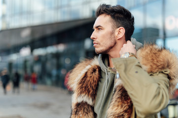 Fashionable man walk outdoors wear  fur jacket with street background - Image