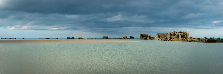 the normandy beaches in france showing ruins and relics from world war II on golden sands and dark...