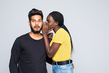 Portrait of cute african woman hair saying secret excited rumors in ear of her indian boyfriend or male friend isolated over white background