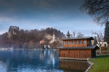 Fototapeta na wymiar Wooden boat house on the lake Bled with the castle and church of St. Martin