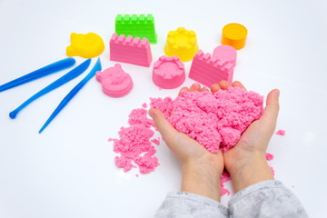 Hands of a kid playing with pink magic sand.