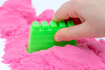 Hands of a kid playing with pink magic sand.