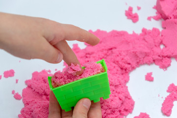 Hands of a kid playing with pink magic sand.