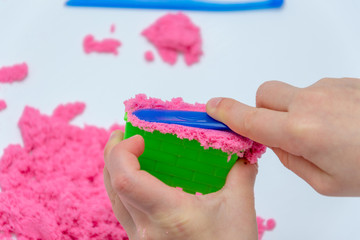 Hands of a kid playing with pink magic sand.