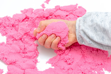 Hands of a kid playing with pink magic sand.