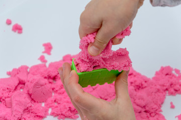 Hands of a kid playing with pink magic sand.