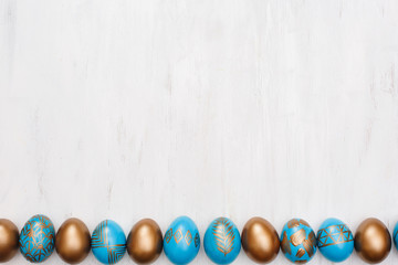 golden decorated easter eggs on white wooden background