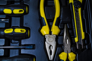 Big tool kit of black and yellow colors for the house in a box. Flat-nose pliers, screw-drivers, stationery knife and nippers. 