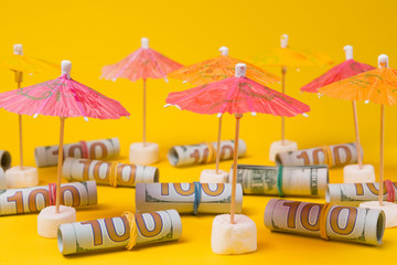 dollars in rolls on a yellow background under multi-colored beach umbrellas, the concept of...