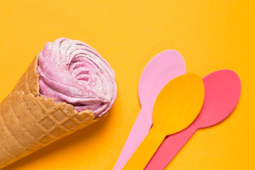 waffle cone with dessert on a yellow background and three multi-colored spoons close by, minimal holiday concept