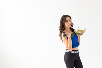 Sport, healthy lifestyle, people concept - young brunette woman with salad and a dumbbell. She is smiling and enjoying the healthy lifestyle on white background with copy space
