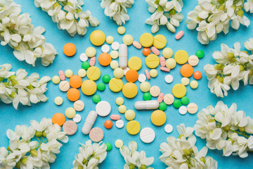 multi-colored pills lie on a blue background surrounded by white acacia inflorescences, the concept...
