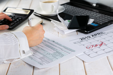 Tax day concept - calculator, calendar, tax form, hands, wood background