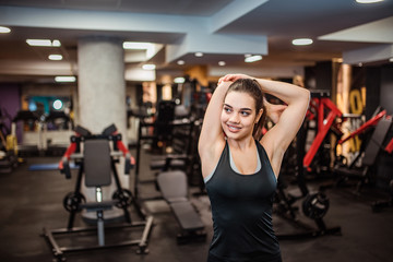 Smiling slim woman in sportswear stretching arms and warming-up in the gym.