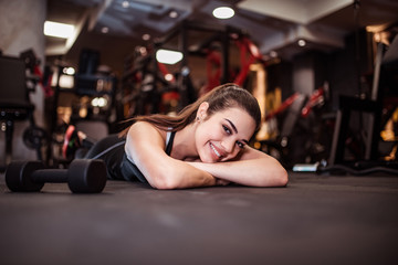 Fototapeta na wymiar Portrait of a smiling athlete relaxing on the floor in the gym, looking at camera.