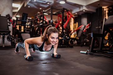 Beautiful smiling girl doing push-up on weights. - obrazy, fototapety, plakaty