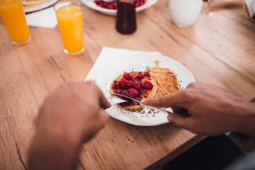Close-up image of man slicing pancakes filled with raspberries on wooden table.
