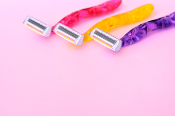 Three woman colorful razors with selective focus on neutral background. New disposable plastic razor with steel blade for daily safety personal shaving on pink background with empty space for text.
