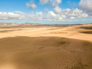 Obraz na płótnie Canvas Aerial view of a desert landscape on the island of Lanzarote, Canary Islands, Spain. Road that crosses a desert. Tongue of black asphalt cutting a desert land. Reliefs on the horizon. Volcanoes