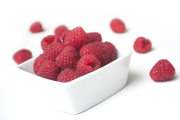 Closeup of raspberries in a white bowl on white background