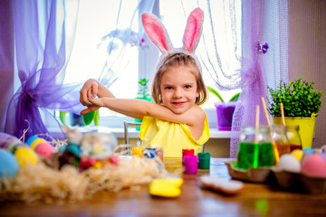colorful painted eggs, flowers in vase. Happy easter girl in bunny ears having fun and painting eggs. small child at home. spring holiday