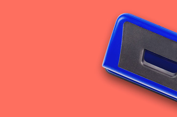 One blue metallic hole puncher on office table or school desk living coral color. Copy space for...