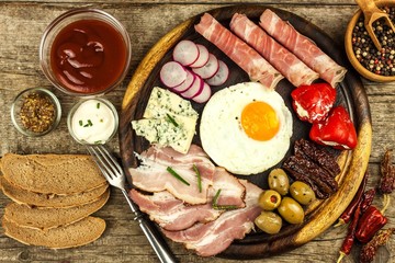 Fried egg on a wooden board. A hearty breakfast with ham and vegetables. Eggs and ham.