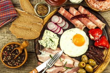 Fried egg on a wooden board. A hearty breakfast with ham and vegetables. Eggs and ham.