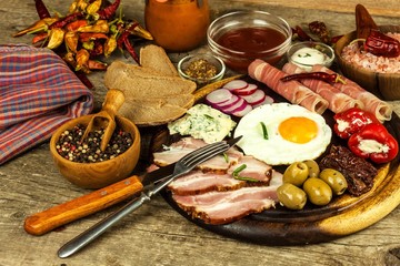Fried egg on a wooden board. A hearty breakfast with ham and vegetables. Eggs and ham.