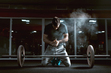 Caucasian muscular man kneeling and clapping hands. In front of him barbell, in background mirror....