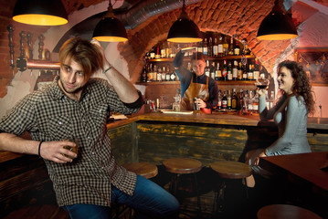 The boy and girl rest in the bar. Couple drinking alcohol. The barman in the background. The concept of love, the first date, valentine day. Many alcoholic beverages on the shelves.