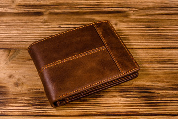 Closed brown leather wallet on wooden table