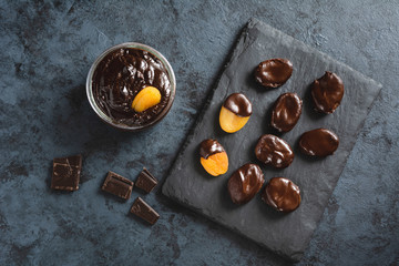 Dried apricots in chocolate on a stone black plate.