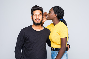 Fototapeta premium Portrait of cute african woman hair saying secret excited rumors in ear of her indian boyfriend or male friend isolated over white background