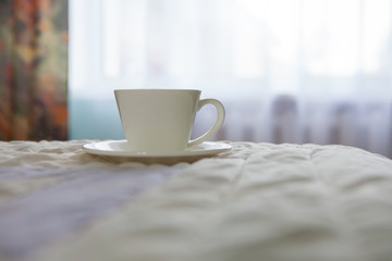 Fototapeta na wymiar morning cup of coffee on the background of the bed and the window