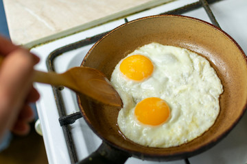 fry eggs in a pan on the stove, stirring with a wooden spatula in your hand